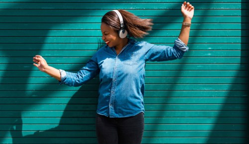 Happy woman dancing and listening to music near a green empty wall outdoor in the city.